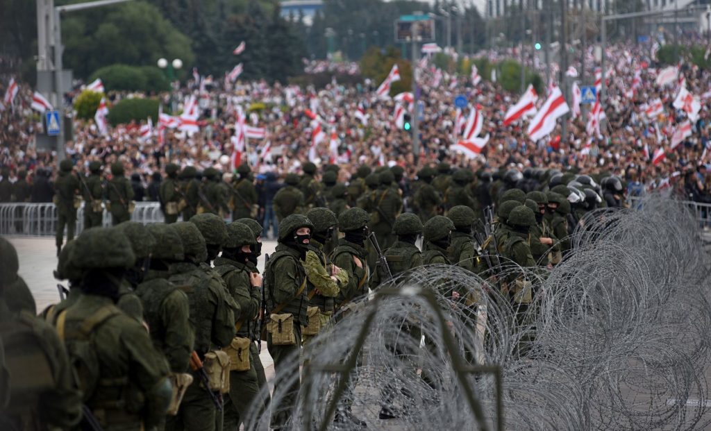 Военные стоят за колючей проволокой, на фоне протестующих людей в Минске 23 августа. Фотограф: Марина Серебрякова / агентство Anadolu через Getty Images